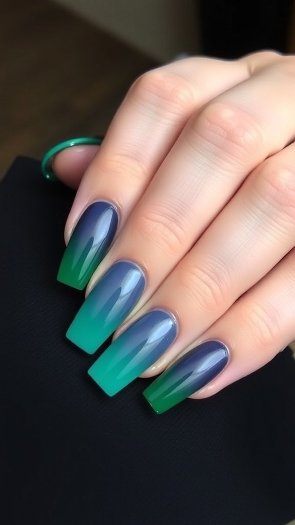 A hand with short square acrylic nails featuring a gradient of deep blue and green colors.