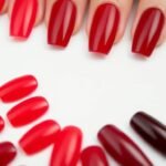 Different shades of red acrylic nails from bright cherry to deep burgundy displayed on nail swatches