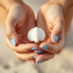 Woman with simple blue ombre beach nails holding a seashell on sandy beach