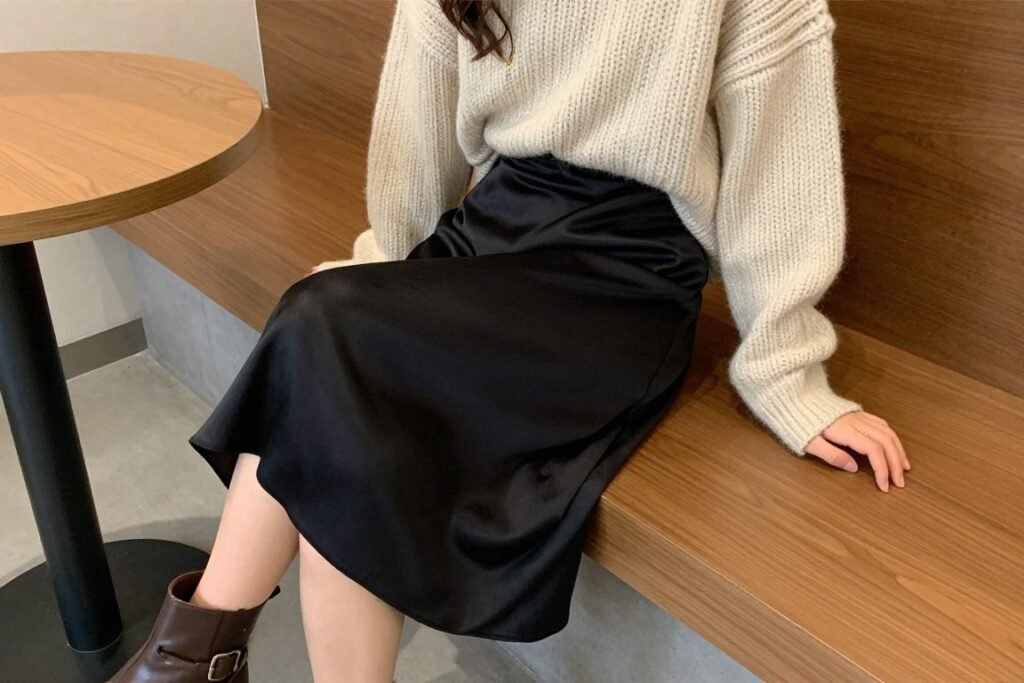 Woman in a black silk skirt paired with an oversized cream sweater and ankle boots