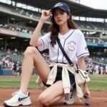 Woman wearing a baseball game outfit with essential items labeled: cap, comfortable shoes, and layers