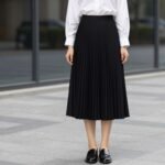 Woman wearing a black pleated skirt with white blouse and minimal accessories
