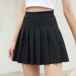 Woman wearing a black tennis skirt paired with a white crop top and sneakers, showcasing the versatile black tennis skirt outfit