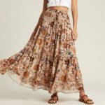 Woman wearing a flowy floral long skirt paired with a white crop top and layered necklaces for a bohemian long skirt outfit