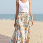 Woman wearing a flowy floral maxi skirt paired with a simple white tank top and straw hat for a perfect summer maxi skirt outfit