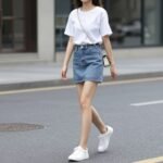 Woman wearing a short denim skirt with a white t-shirt and sneakers for a casual daytime look