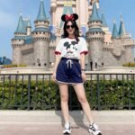 Woman wearing a stylish Mickey Mouse t-shirt and comfortable shorts standing in front of Cinderella Castle at Disney World