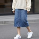 Woman wearing a stylish midi jean skirt outfit with white sneakers and oversized sweater