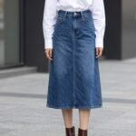Woman wearing classic blue denim midi skirt paired with white button-down shirt and ankle boots